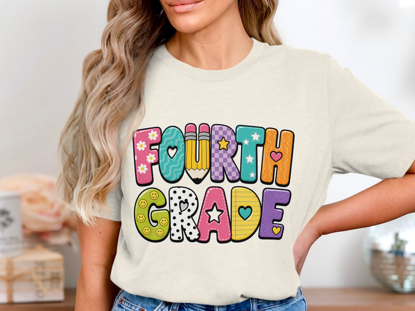 Colorful "Fourth Grade" text with playful patterns and school-themed elements on a cream t-shirt.