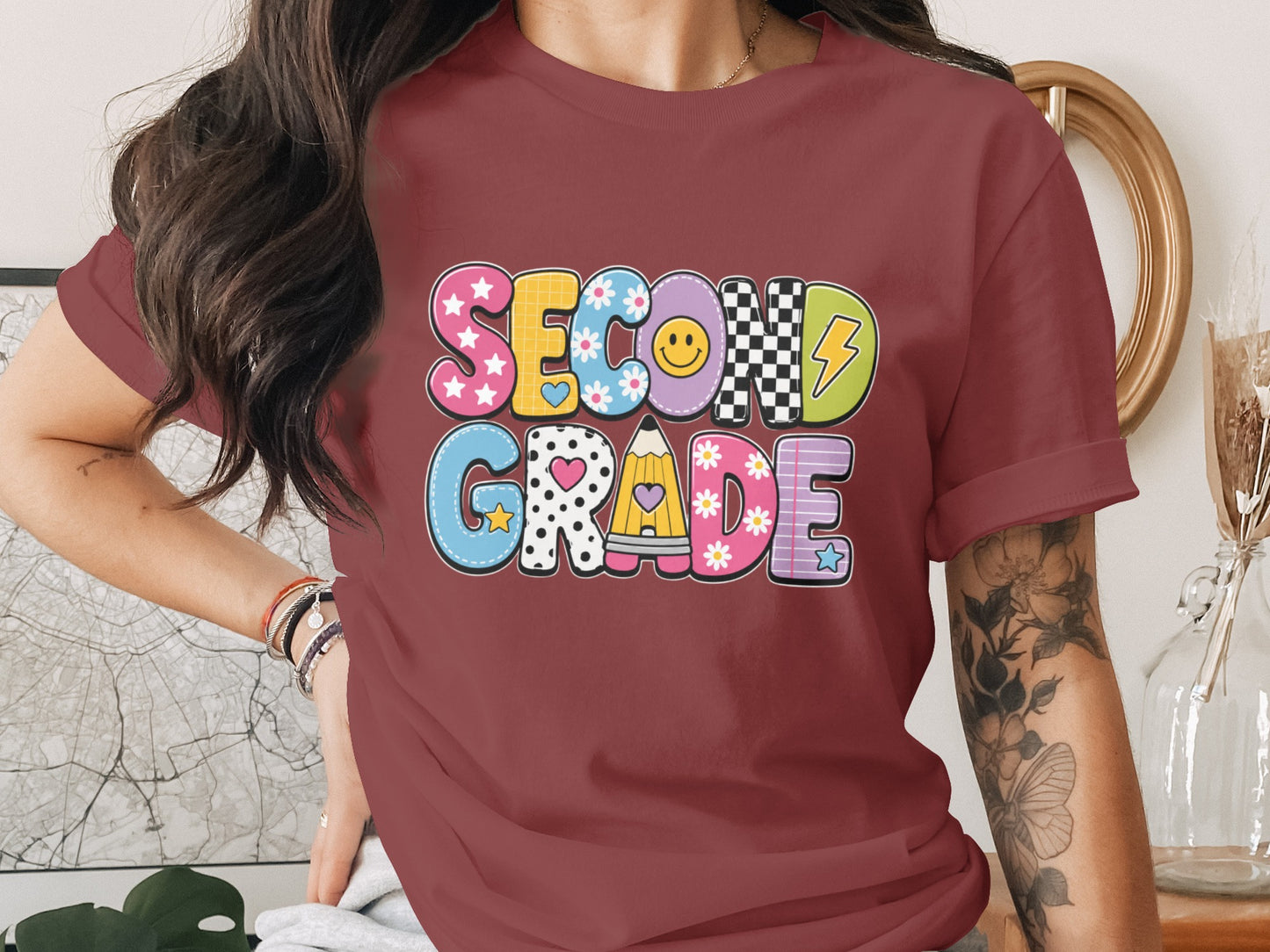 Maroon t-shirt with colorful "SECOND GRADE" text featuring patterns and school icons.