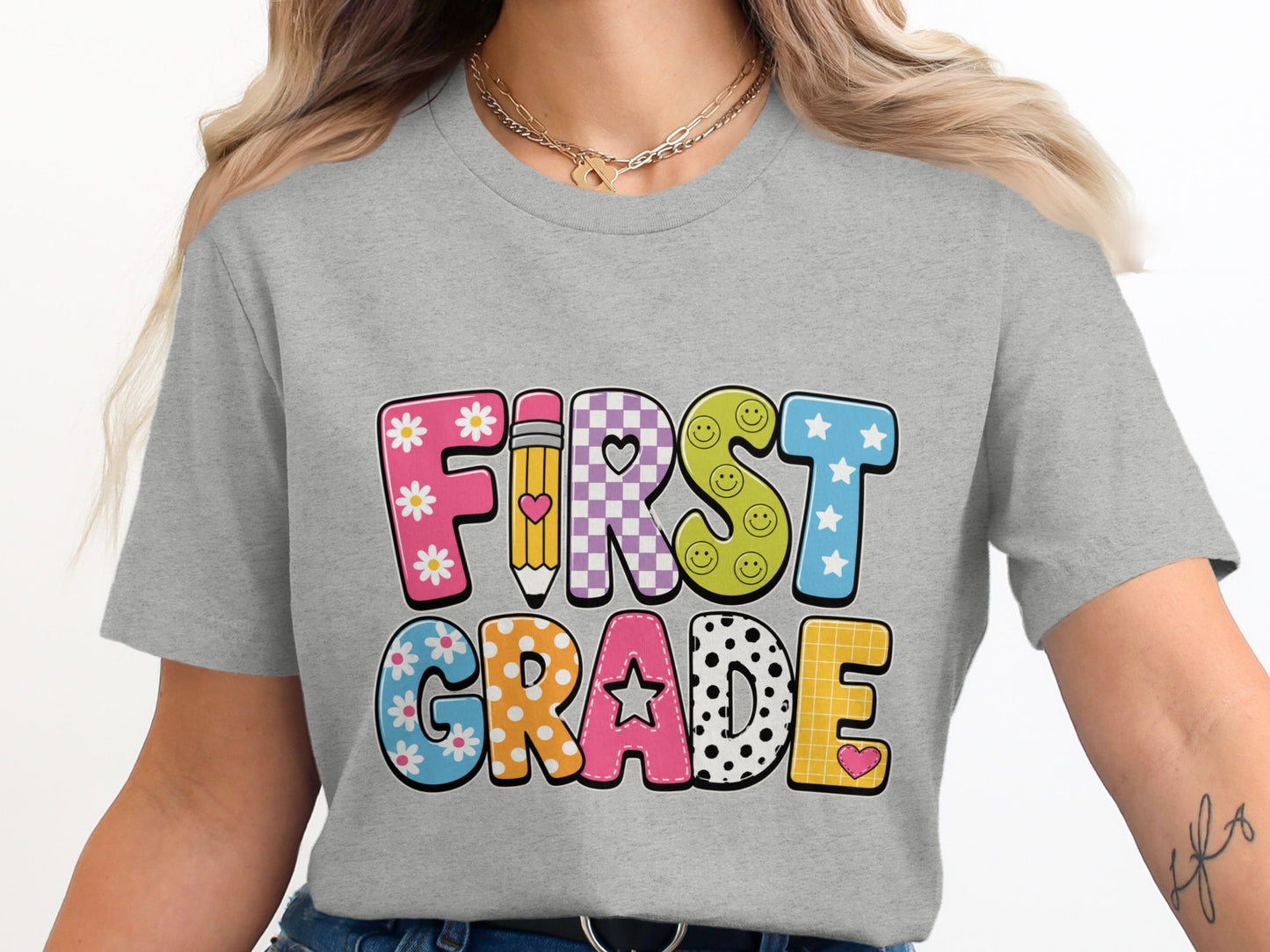 Grey t-shirt with colorful "First Grade" text featuring flowers, smiley faces, and polka dots.
