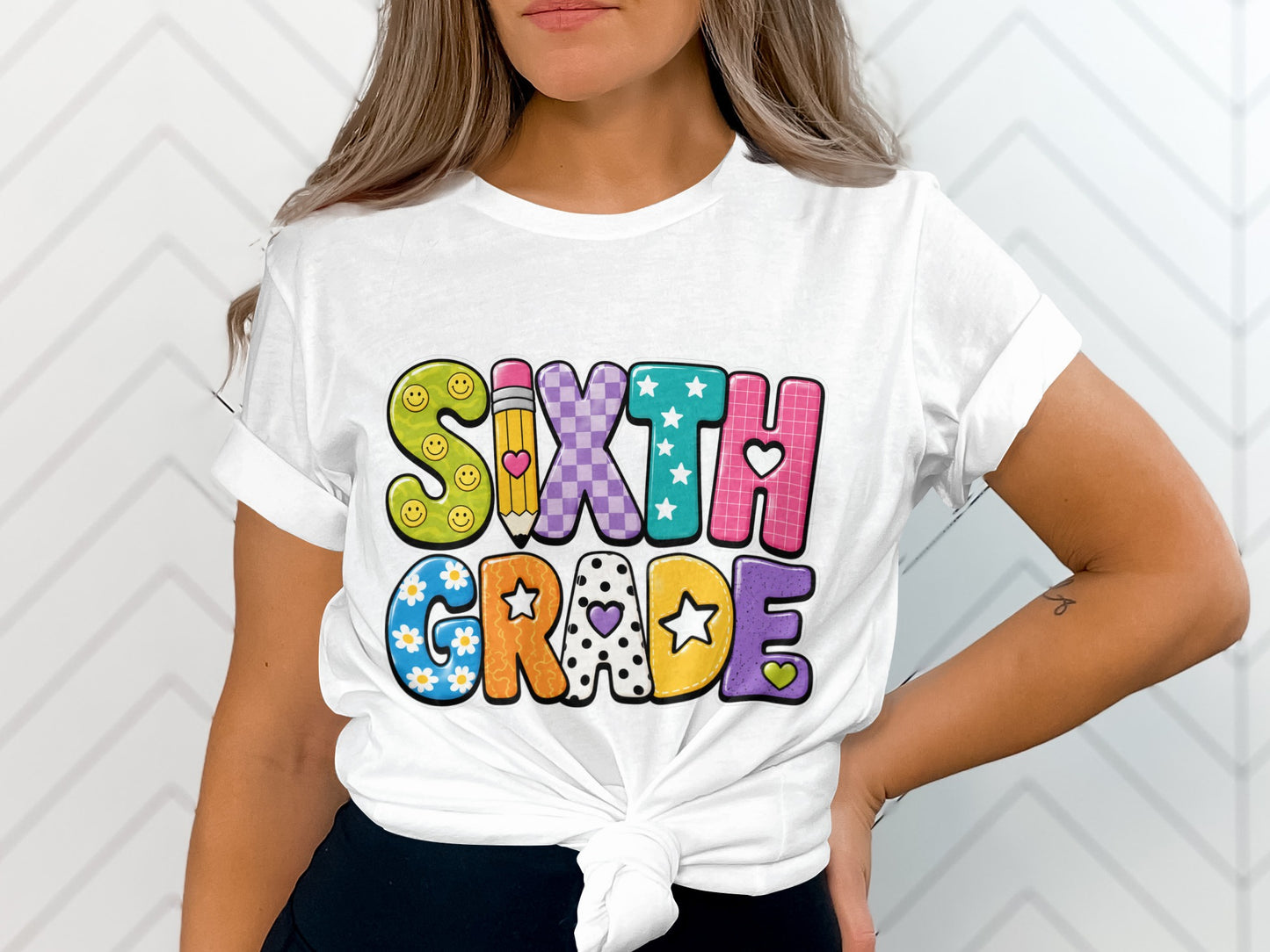 White t-shirt with colorful "SIXTH GRADE" text design featuring smiley faces, pencil, hearts, and stars.