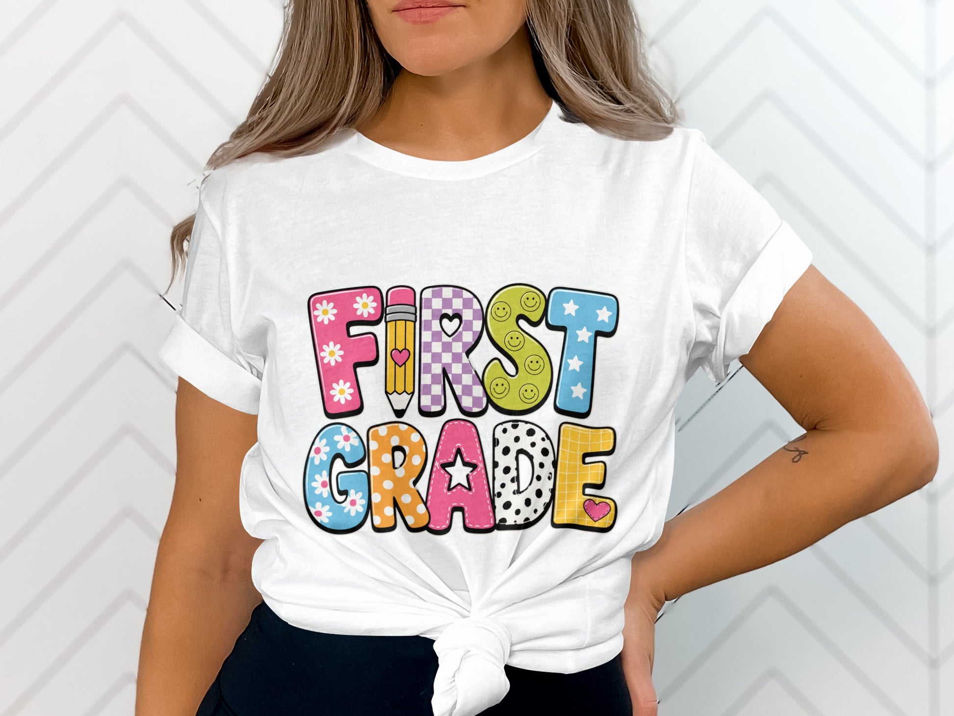 White t-shirt with "FIRST GRADE" text in colorful, patterned block letters.