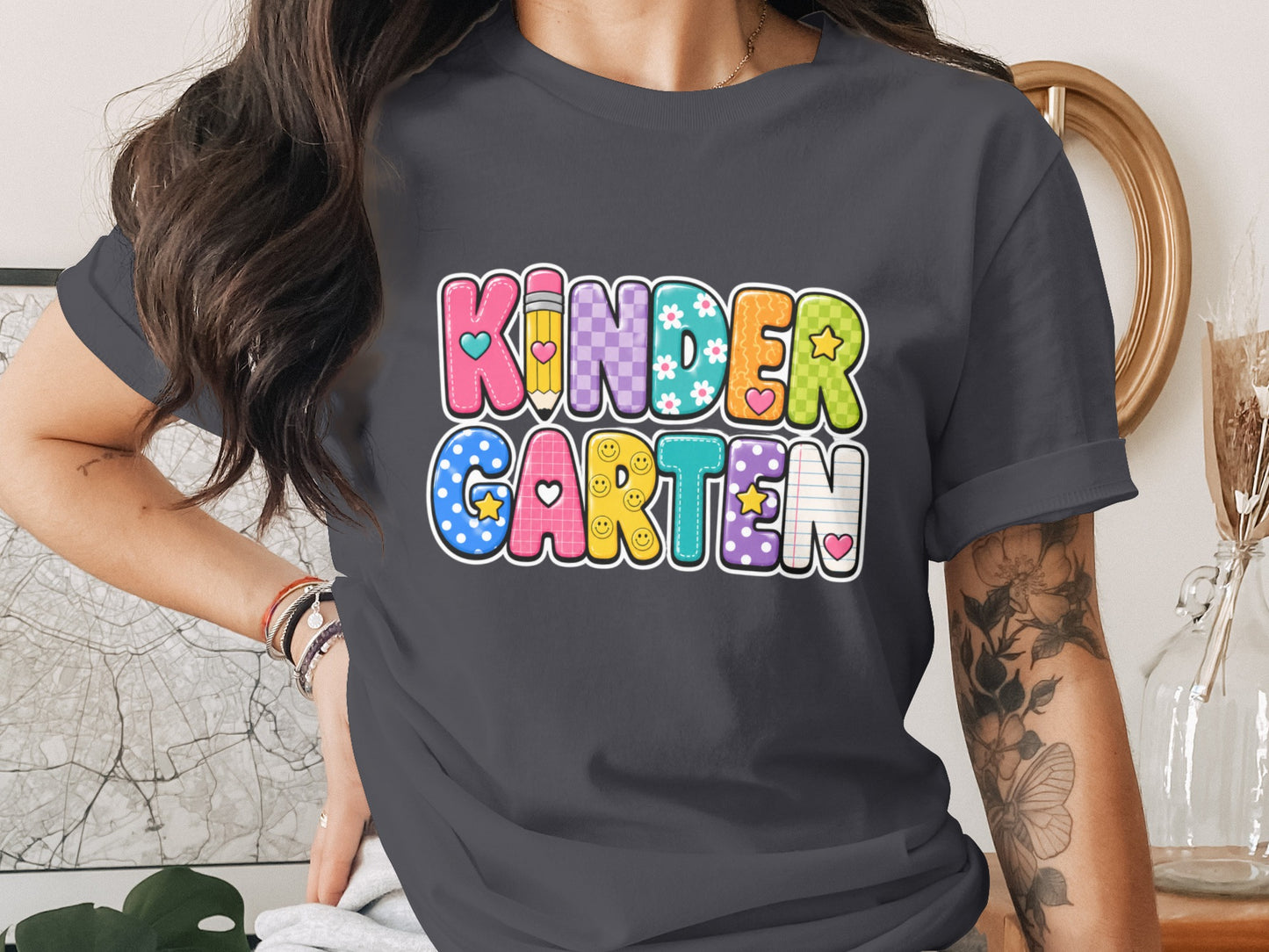 KINDERGARTEN text in colorful, patterned block letters with cute decorations on a gray t-shirt.