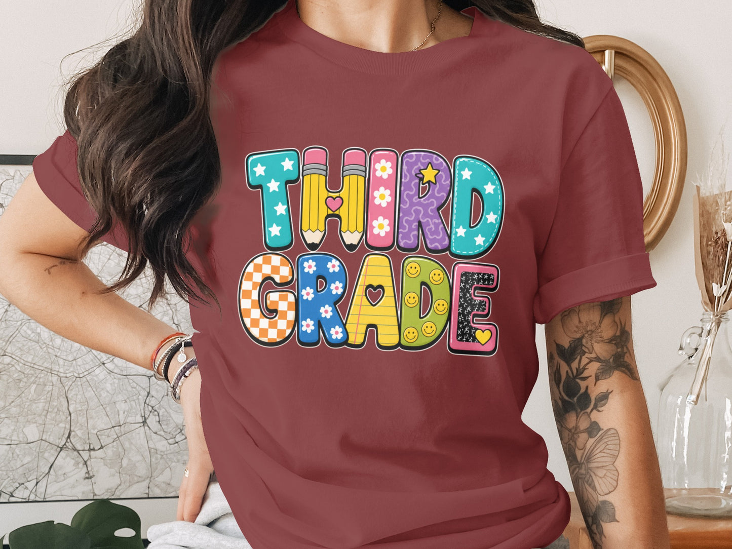 Maroon t-shirt with colorful "THIRD GRADE" text design featuring pencils, flowers, and smiley faces.