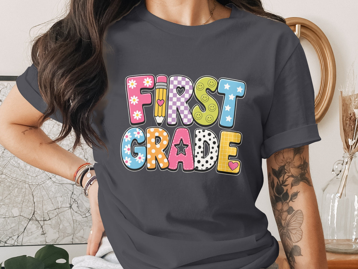 Colorful "FIRST GRADE" text with decorative patterns on a charcoal t-shirt.