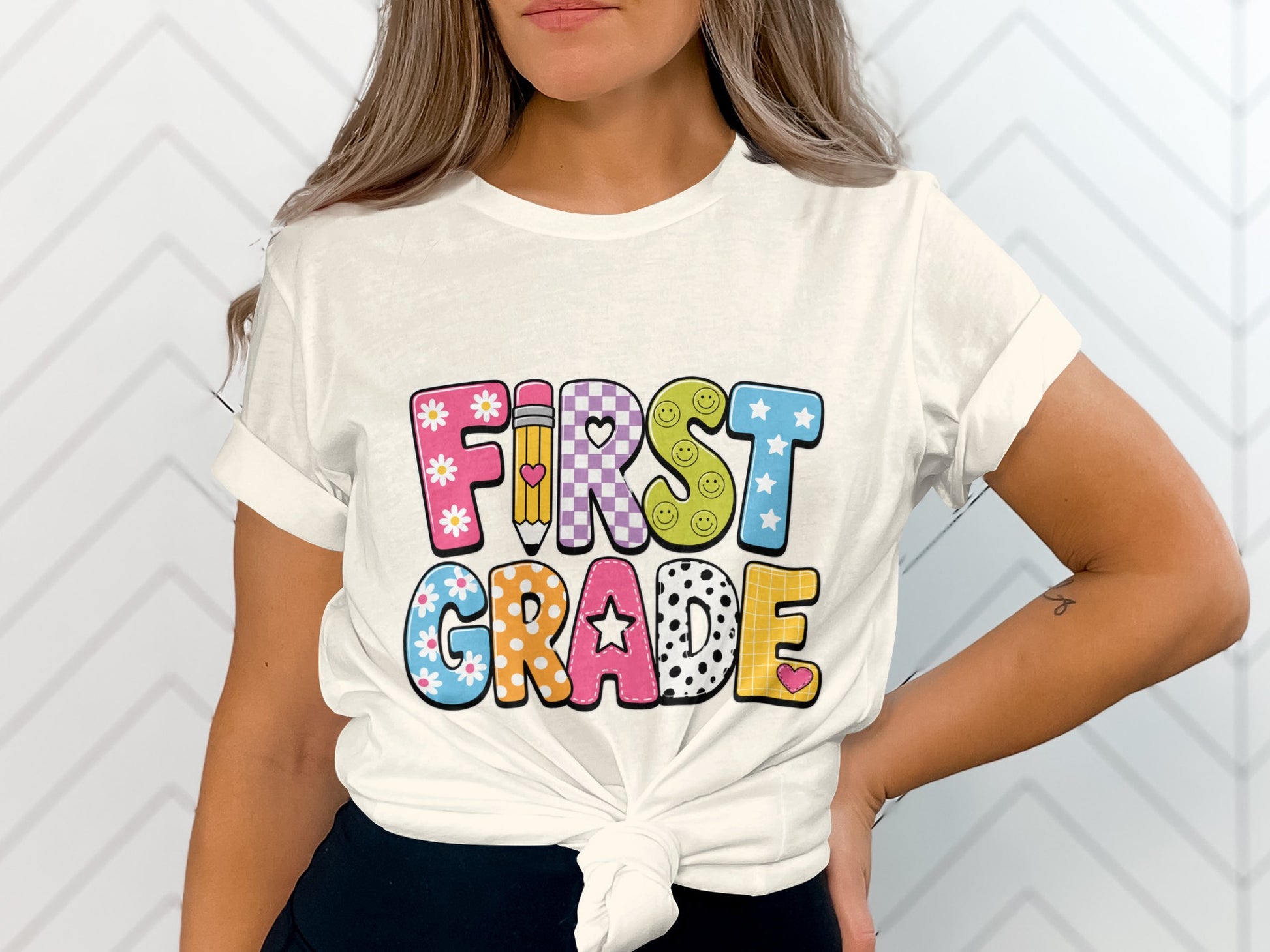 White t-shirt with colorful "FIRST GRADE" text overlay featuring stars, flowers, and smiley faces.
