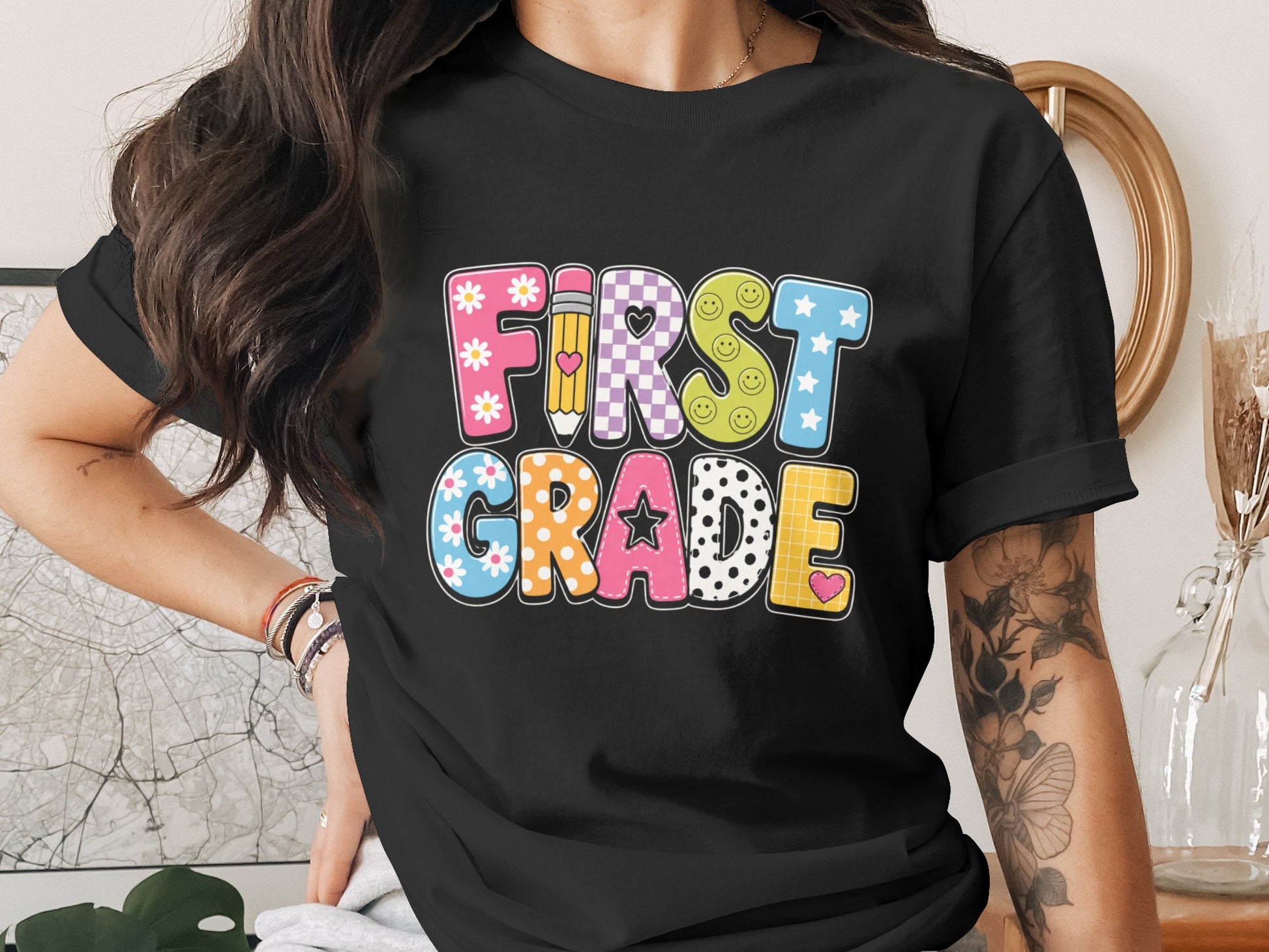 Black t-shirt with colorful "First Grade" text featuring patterns and school icons.