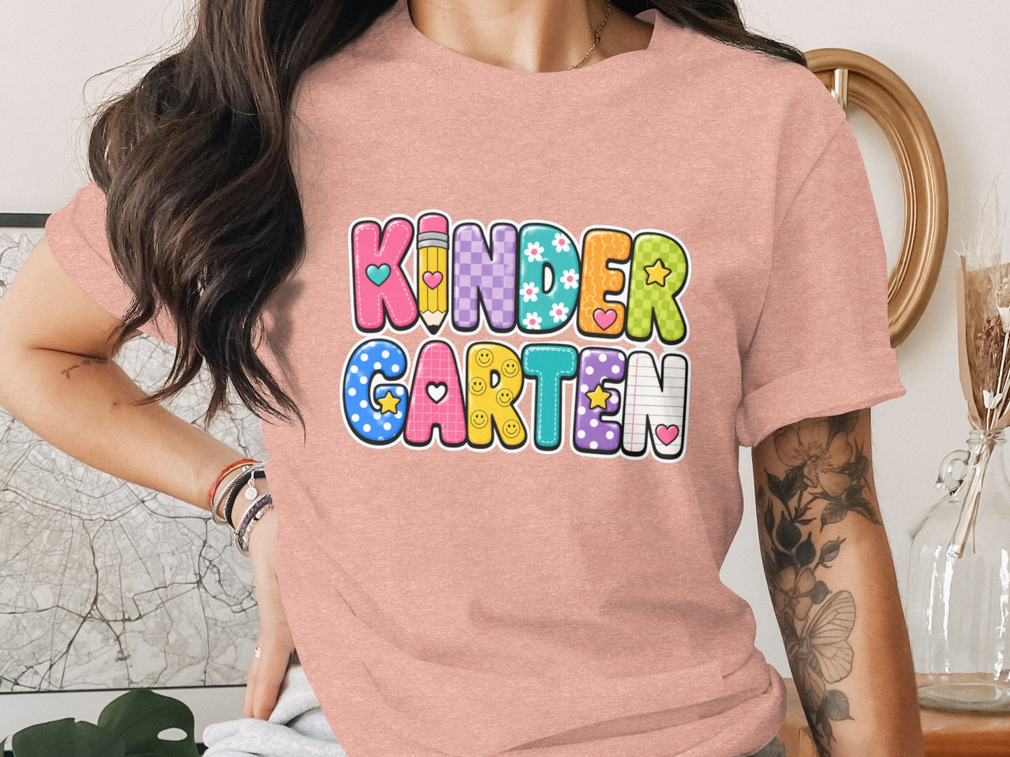 A person wearing a pink t-shirt with "KINDERGARTEN" in colorful, patterned letters.