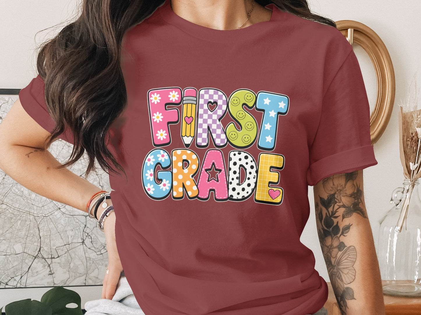 "First Grade" text graphic with patterned letters on a maroon t-shirt.