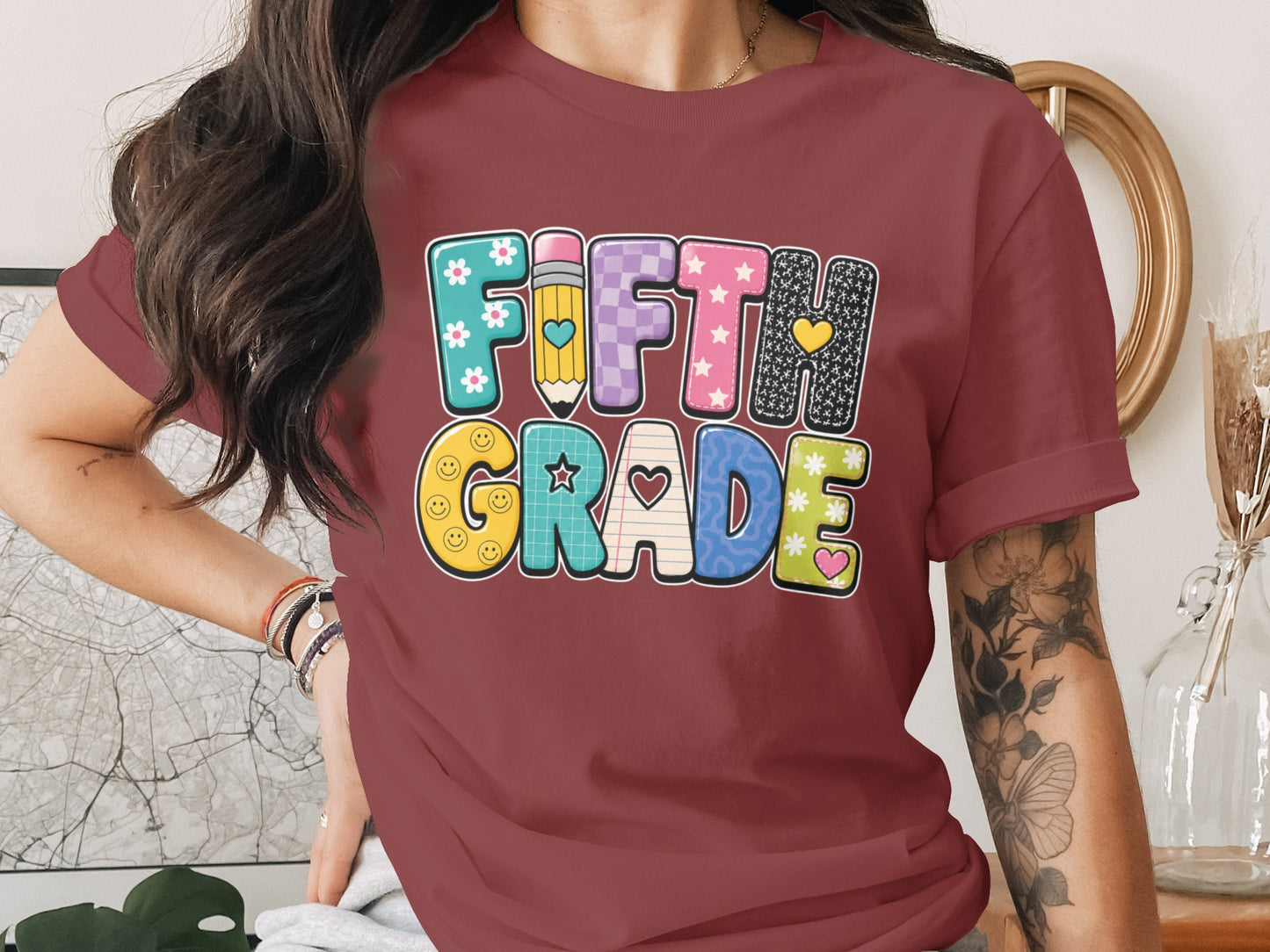 Maroon t-shirt graphic with colorful "FIFTH GRADE" text and school-themed embellishments.